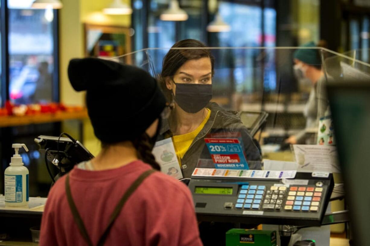 Zaida MacDonald completes a purchase at the New Seasons Market at Fisher&#039;s Landing on Tuesday. New Seasons uses plexiglass screens and demands customers wear cloth masks to prevent the spread of the coronavirus, particularly as holiday season approaches.