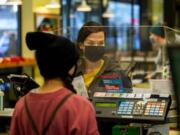 Zaida MacDonald completes a purchase at the New Seasons Market at Fisher&#039;s Landing on Tuesday. New Seasons uses plexiglass screens and demands customers wear cloth masks to prevent the spread of the coronavirus, particularly as holiday season approaches.