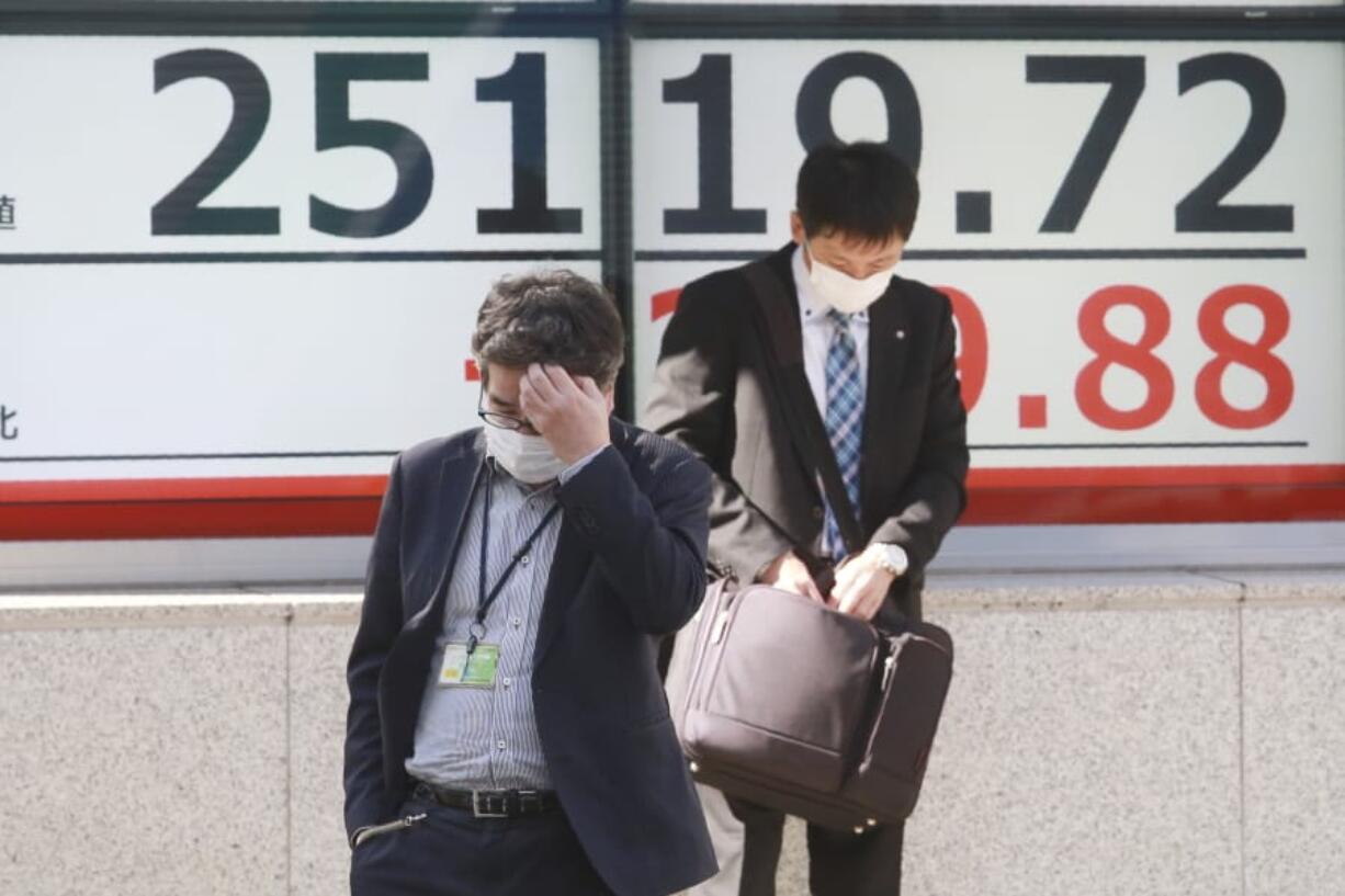 People walk by an electronic stock board of a securities firm in Tokyo, Tuesday, Nov. 10, 2020. Asian stock markets rose for second day Tuesday on hopes for progress toward a possible coronavirus vaccine that might allow the world to revive manufacturing, shopping and normal life.