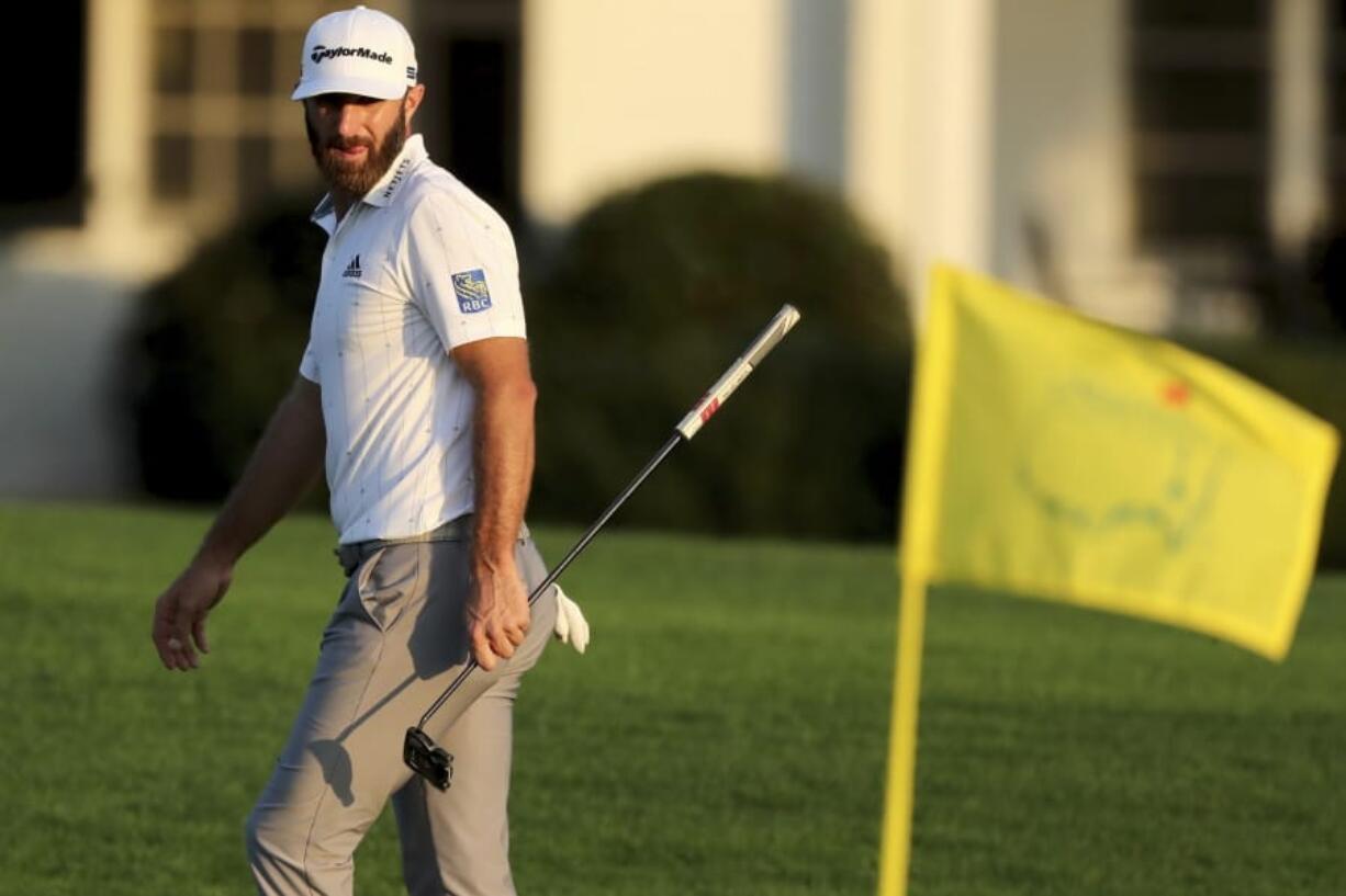 Dustin Johnson looks over his shot on the 18th green next to the Masters yellow flag during the third round of the Masters golf tournament Saturday, Nov. 14, 2020, in Augusta, Ga.