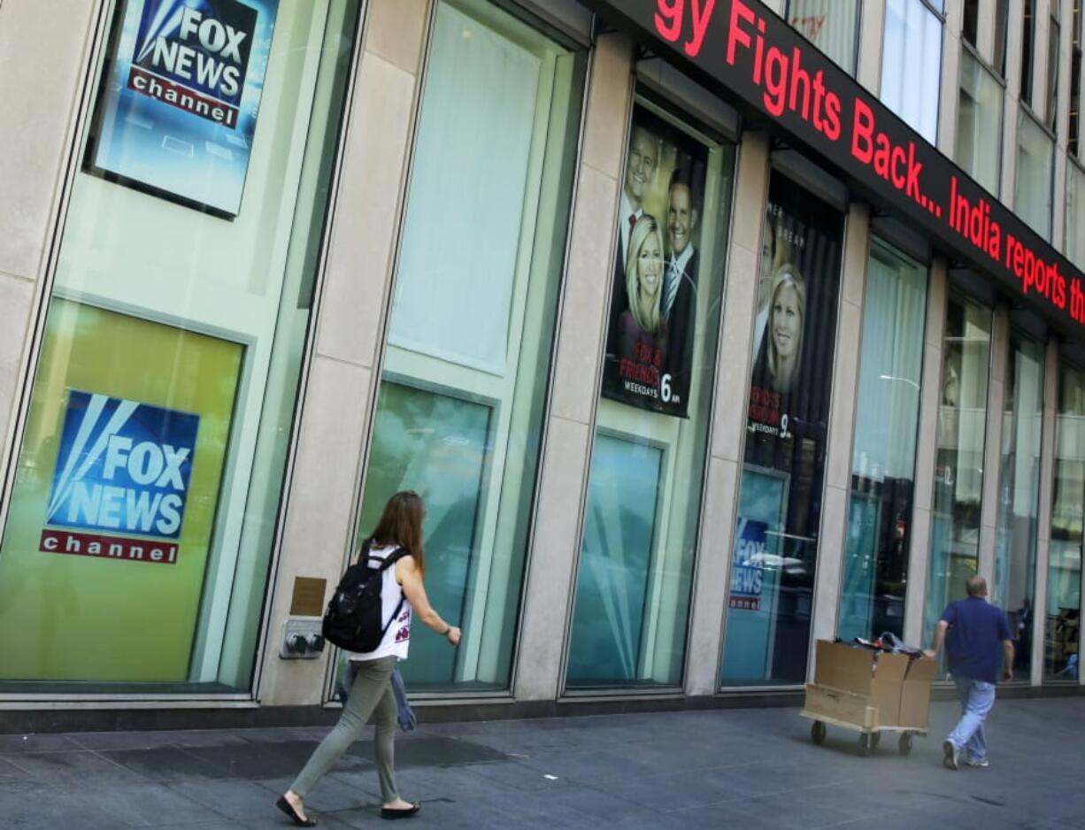 FILE- People pass the News Corporation headquarters building and Fox News studios in New York on Aug. 1, 2017. Several Fox News Channel executives and on-air personalities were exposed last week to a person on a private plane who later tested positive for COVID-19. It has led to some restrictions at the network. Anchor Bret Baier said Monday that he&#039;s tested negative three times in the wake of the flight and will be doing his nightly news show from home this week.