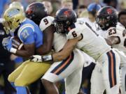 FILE - In this Oct. 5, 2019, file photo, UCLA running back Joshua Kelley, left, is tackled by Oregon State linebackers Hamilcar Rashed Jr. (9) and John McCartan (6) during the first half of an NCAA college football game in Pasadena, Calif. While the offense is still coming together with presumed starting quarterback Tristan Gebbia, it&#039;s Oregon State&#039;s defense that should worry opponents.