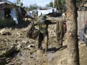 A policeman carries his belongings across debris and muds at the typhoon-damaged Kasiglahan village in Rodriguez, Rizal province, Philippines on Friday, Nov. 13, 2020. Thick mud and debris coated many villages around the Philippine capital Friday after Typhoon Vamco caused extensive flooding that sent residents fleeing to their roofs and killing dozens of people.