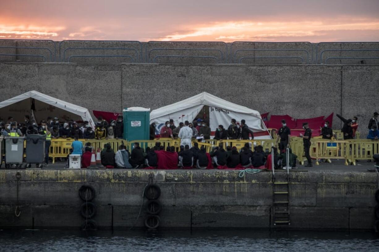 Migrants sit in Arguineguin port after their rescue in Gran Canaria island, Spain on Tuesday, Nov. 24, 2020. Spanish rescue services said Wednesday at least seven people died after a migrant boat carrying more than 30 people hit rocks close to a small port on the Canary Island of Lanzarote. Many of the rescued were taken to the Arguineguin dock on the southwestern coast of Gran Canaria island, where several thousand people of different origin are being kept, some in tents.