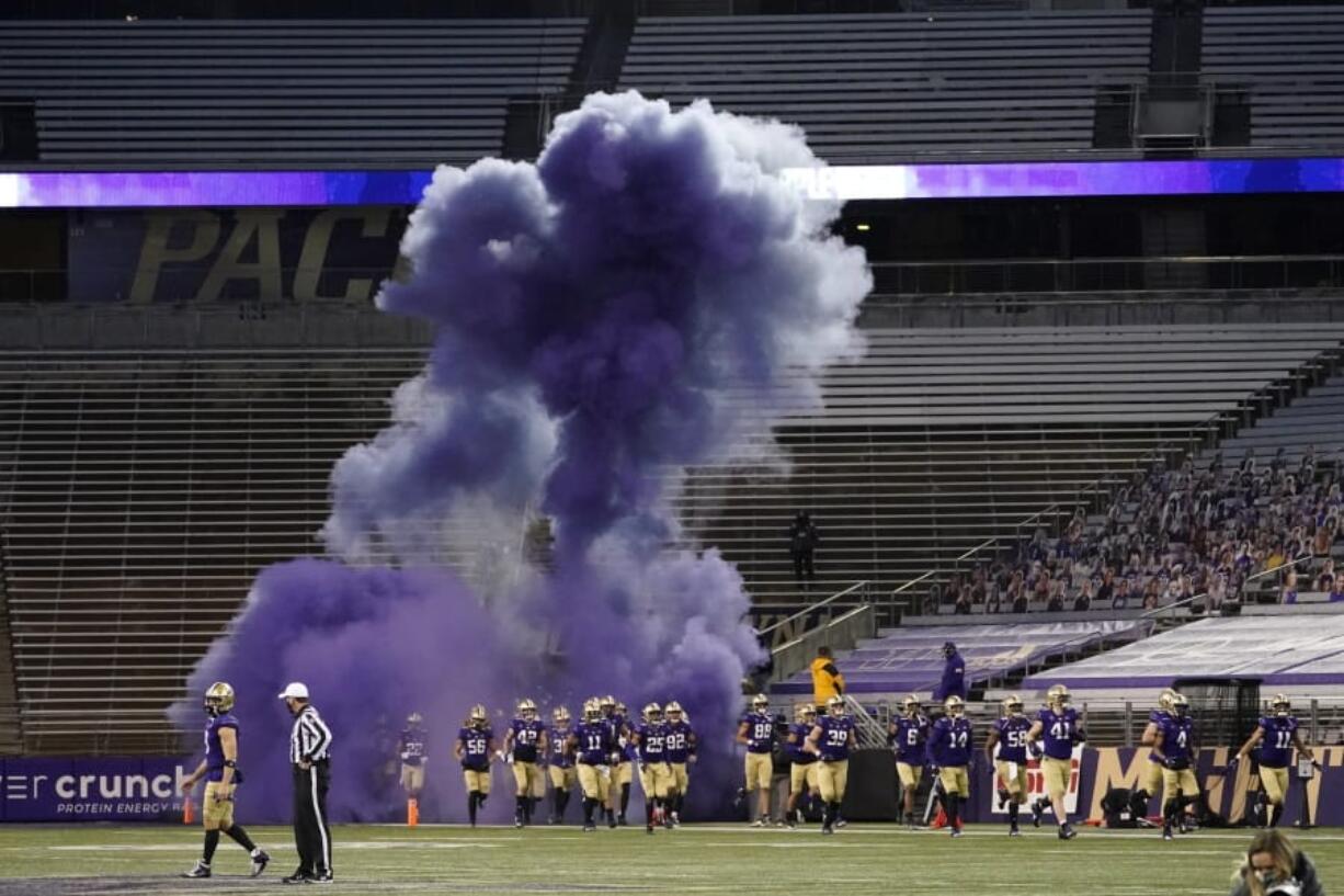 Washington players run out of a tunnel through a cloud of purple smoke in front of empty seats at Husky Stadium before an NCAA college football game against Utah, Saturday, Nov. 28, 2020, in Seattle. Due to the COVID-19 pandemic, no fans were in attendance at the game. (AP Photo/Ted S.