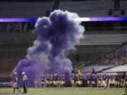 Washington players run out of a tunnel through a cloud of purple smoke in front of empty seats at Husky Stadium before an NCAA college football game against Utah, Saturday, Nov. 28, 2020, in Seattle. Due to the COVID-19 pandemic, no fans were in attendance at the game. (AP Photo/Ted S.