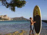 In this photo provided by Yoko Liriano, Bryant de Venecia poses for a photo with his paddleboard in Honolulu, Wednesday, Nov. 11, 2020. He started stand-up paddle-boarding when there were fewer tourists coming to Hawaii during the pandemic. He&#039;s among the Hawaii residents feeling ambivalence toward tourists returning now that the state is allowing incoming travelers to bypass a 14-day quarantine with a negative COVID-19 test.