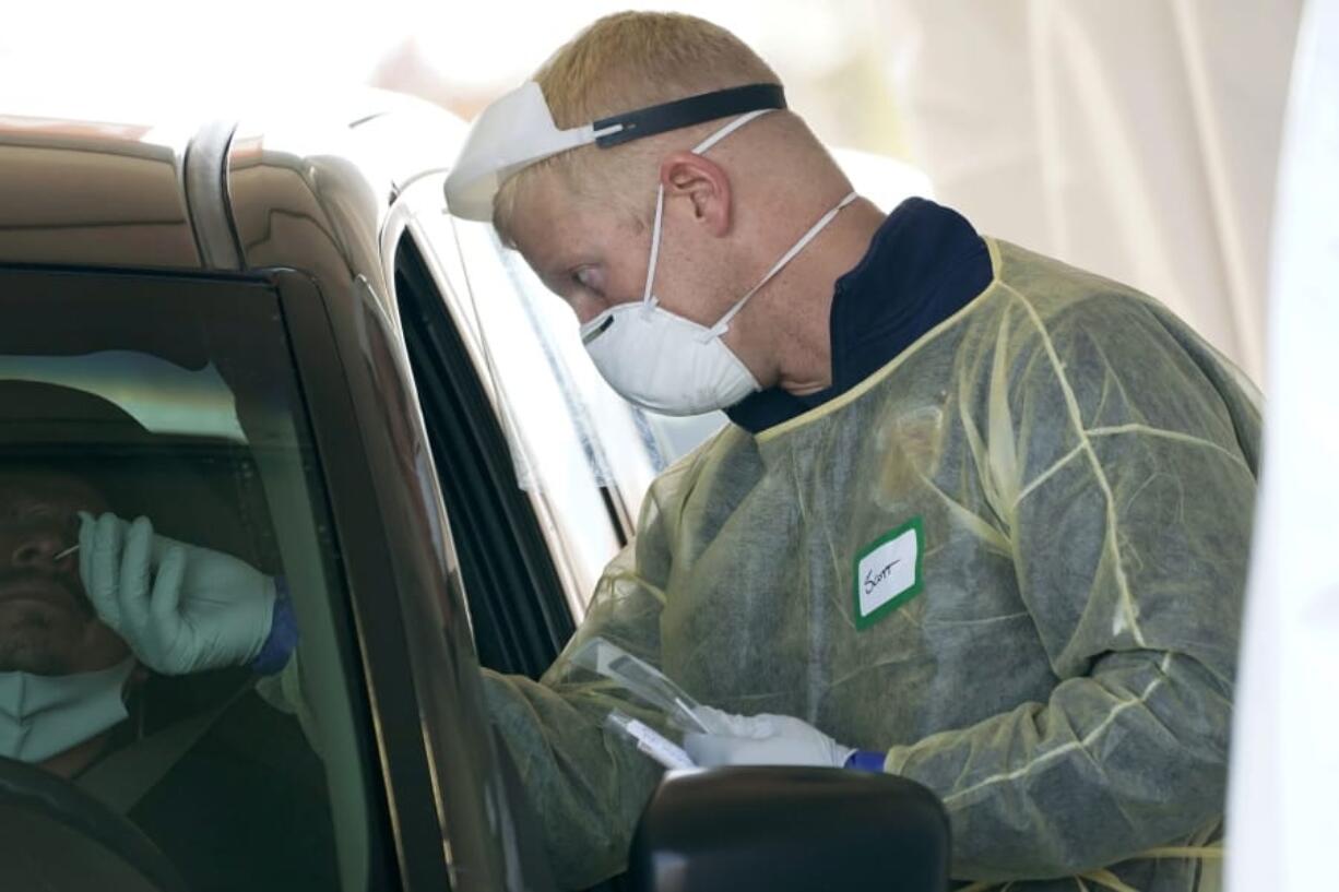 FILE - In this Oct. 28, 2020, file photo, a worker wearing gloves, a face shield, a mask, and other PPE administers a COVID-19 test at a King County coronavirus testing site in Auburn, Wash., south of Seattle. The latest surge in U.S. coronavirus cases appears to be larger and more widespread than the two previous ones, and it is all but certain to get worse. But experts say there are also reasons to think the nation is better able to deal with the virus than before, with the availability of better treatments, wider testing and perhaps greater political will. (AP Photo/Ted S.