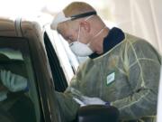 FILE - In this Oct. 28, 2020, file photo, a worker wearing gloves, a face shield, a mask, and other PPE administers a COVID-19 test at a King County coronavirus testing site in Auburn, Wash., south of Seattle. The latest surge in U.S. coronavirus cases appears to be larger and more widespread than the two previous ones, and it is all but certain to get worse. But experts say there are also reasons to think the nation is better able to deal with the virus than before, with the availability of better treatments, wider testing and perhaps greater political will. (AP Photo/Ted S.