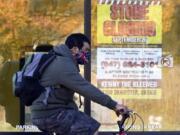 FILE - In this Friday, Nov. 6, 2020, file photo, a man wearing a face mask rides a bicycle past a closed store in Wilmette, Ill. States in the U.S. are renewing their push for more federal money to deal with the fallout from the coronavirus outbreak and to help them distribute a vaccine when one becomes widely available sometime in 2021. (AP Photo/Nam Y.