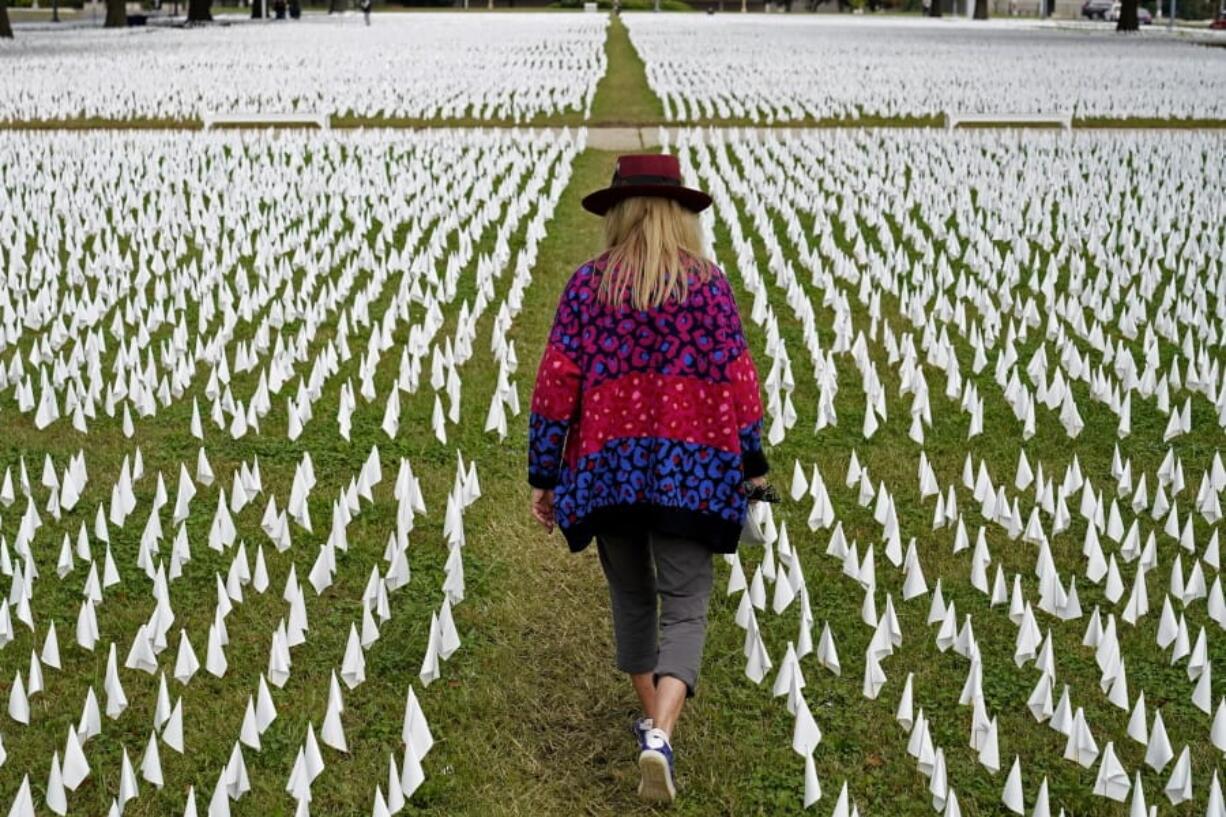 FILE - In this Oct. 27, 2020, Artist Suzanne Brennan Firstenberg walks among thousands of white flags planted in remembrance of Americans who have died of COVID-19 near Robert F. Kennedy Memorial Stadium in Washington. Regardless of the presidential election outcome, a vexing issue remains to be decided: Will the U.S. be able to tame a perilous pandemic that is surging as holidays, winter and other challenges approach? Public health experts fear the answer is no, at least in the short term, with potentially dire consequences.