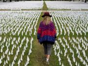 FILE - In this Oct. 27, 2020, Artist Suzanne Brennan Firstenberg walks among thousands of white flags planted in remembrance of Americans who have died of COVID-19 near Robert F. Kennedy Memorial Stadium in Washington. Regardless of the presidential election outcome, a vexing issue remains to be decided: Will the U.S. be able to tame a perilous pandemic that is surging as holidays, winter and other challenges approach? Public health experts fear the answer is no, at least in the short term, with potentially dire consequences.