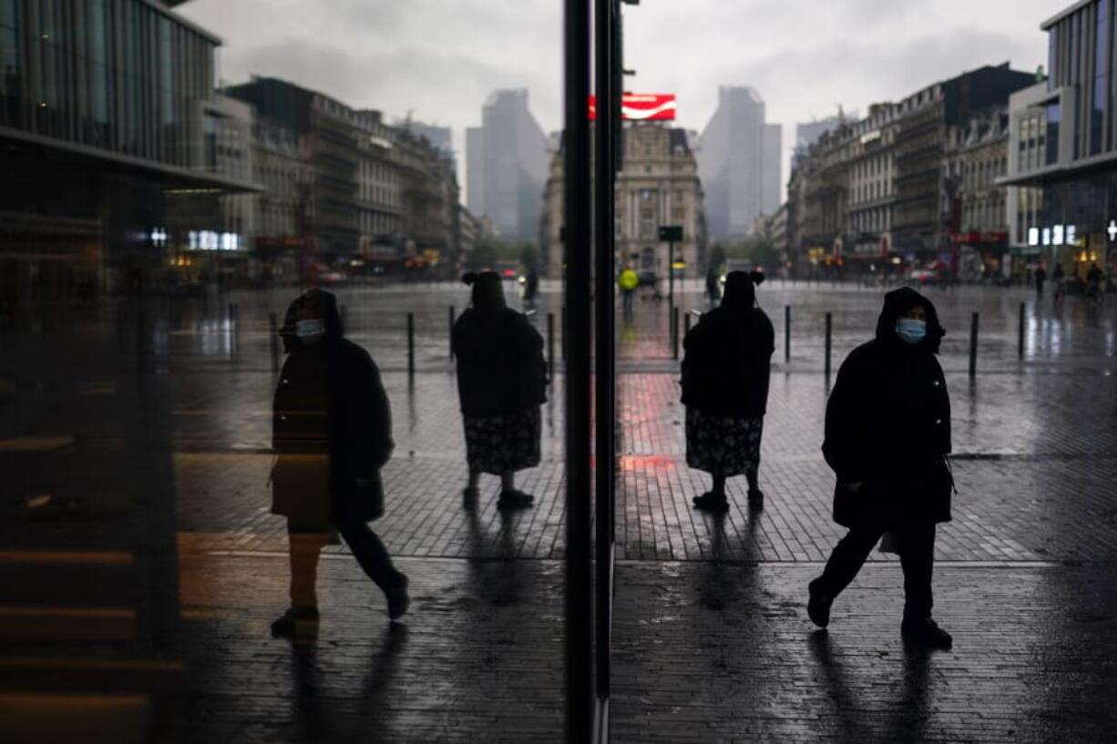 Passers-by, wearing face masks to prevent the spread of the coronavirus COVID-19, walk along a commercial area during a rainy autumn day in Brussels, Tuesday, Nov. 10, 2020.