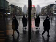 Passers-by, wearing face masks to prevent the spread of the coronavirus COVID-19, walk along a commercial area during a rainy autumn day in Brussels, Tuesday, Nov. 10, 2020.