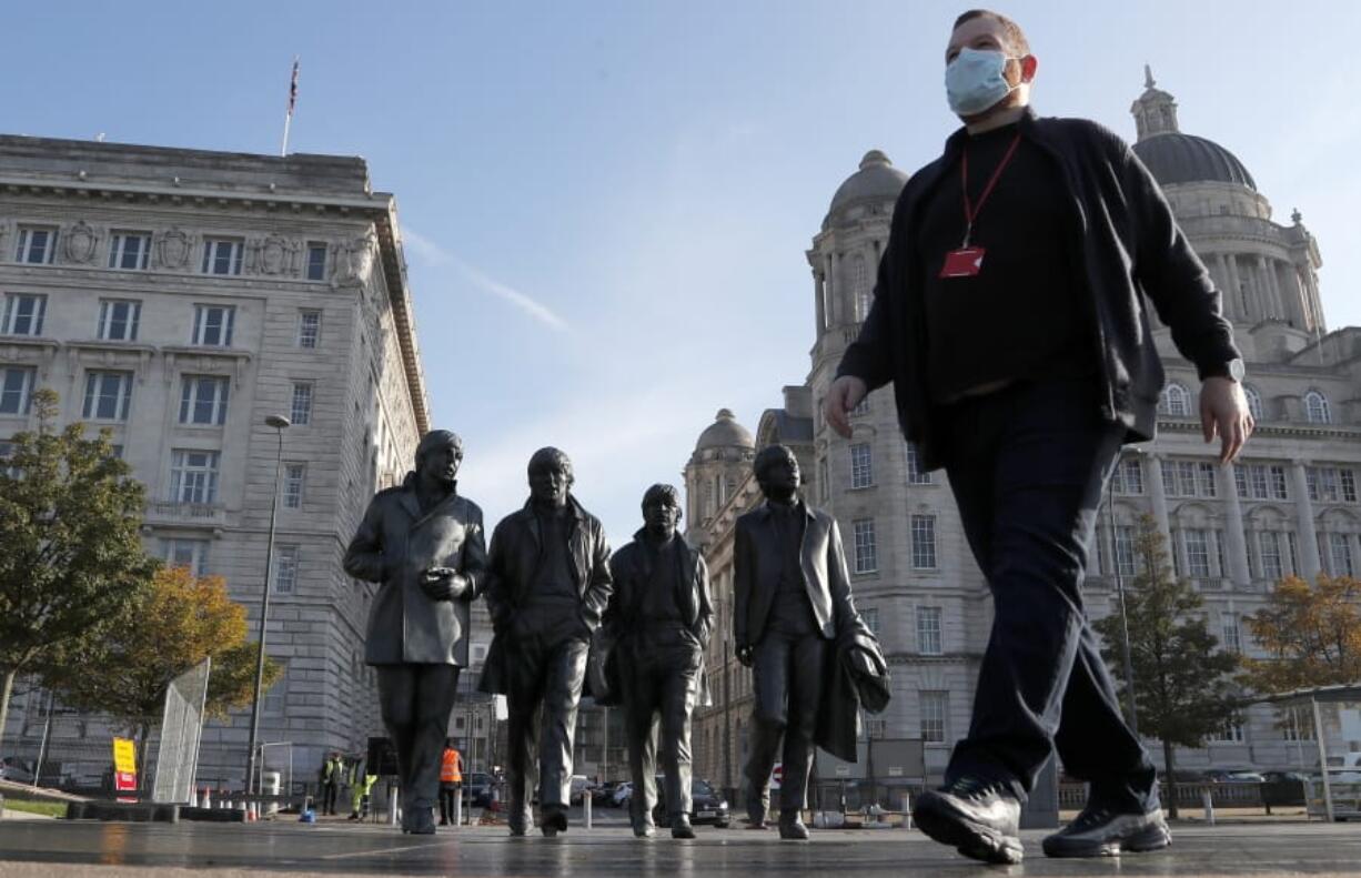 FILE - In this Wednesday, Oct. 14, 2020  file photo, a man wearing a face mask walks past a statue of the Beatles, as new measures across the region are set to come into force in Liverpool, England. A half-million people in the city of Liverpool will be regularly tested for COVID-19 in Britain&#039;s first citywide trial of widespread, rapid testing that the government hopes will be a new weapon in combatting the pandemic. The government said in a statement Tuesday that testing will begin later this week at sites throughout the city using a variety of technologies, including new methods that can provide results in an hour or less. Everyone who lives or works in the city in northwestern England will be offered the test, regardless of whether they have symptoms.