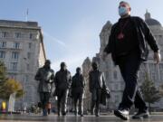 FILE - In this Wednesday, Oct. 14, 2020  file photo, a man wearing a face mask walks past a statue of the Beatles, as new measures across the region are set to come into force in Liverpool, England. A half-million people in the city of Liverpool will be regularly tested for COVID-19 in Britain&#039;s first citywide trial of widespread, rapid testing that the government hopes will be a new weapon in combatting the pandemic. The government said in a statement Tuesday that testing will begin later this week at sites throughout the city using a variety of technologies, including new methods that can provide results in an hour or less. Everyone who lives or works in the city in northwestern England will be offered the test, regardless of whether they have symptoms.