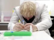 Britain&#039;s Prime Minister Boris Johnson, wearing a mask because of the coronavirus,  has a close look at a sample at the Lateral Flow Testing Laboratory during a visit to the Public Health England site at Porton Down science park near Salisbury, southern England, on Friday Nov. 27, 2020.