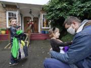 Alex Stonehill gets a goodbye from his daughter Helenore, 2, as her brother Malcolm, 4, motions to a friend arriving at the Community Day Center for Children on Thursday, Oct. 29, 2020, in Seattle. As more families make the jump back to group day care this fall in an attempt to restart lives and careers, many parents, pediatricians and care operators are finding that new, pandemic-driven rules offer a much-needed layer of safety but also seem incompatible with the germy reality of childhood.