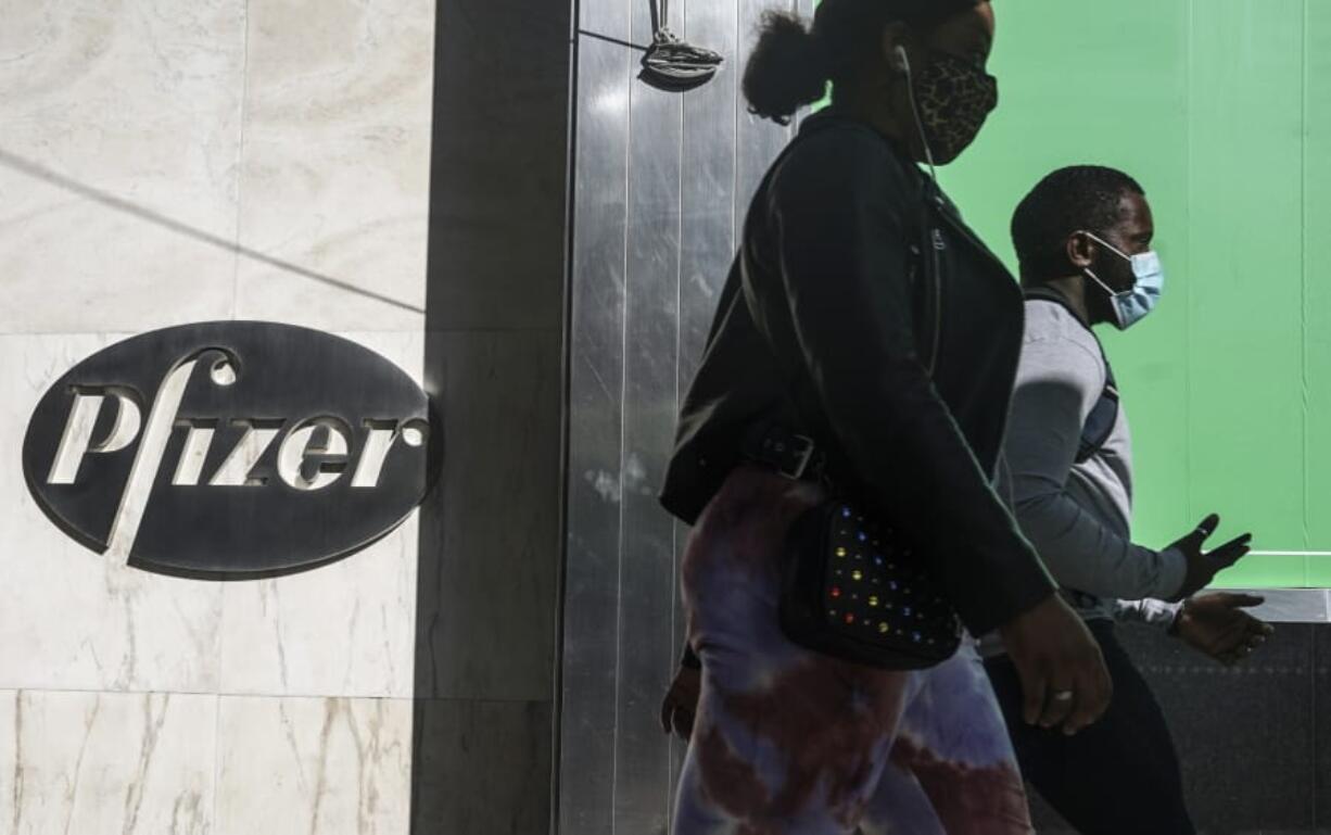 FILE - In this Nov. 9, 2020, file photo, pedestrians walk past Pfizer world headquarters in New York. Pfizer said Friday, Nov. 20, 2020, it is asking U.S. regulators to allow emergency use of its COVID-19 vaccine, starting the clock on a process that could bring limited first shots as early as next month and eventually an end to the pandemic -- but not until after a long, hard winter.