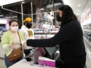 Cashier Druhan Parker, right, works behind a plexiglass shield Thursday, Nov. 19, 2020, as he checks out shoppers Cassie Howard, left, and Paris Black at an in Chicago. The accelerating surge of coronavirus cases across the U.S. is causing an existential crisis for America&#039;s retailers and spooking their customers just as the critically important holiday shopping season nears.