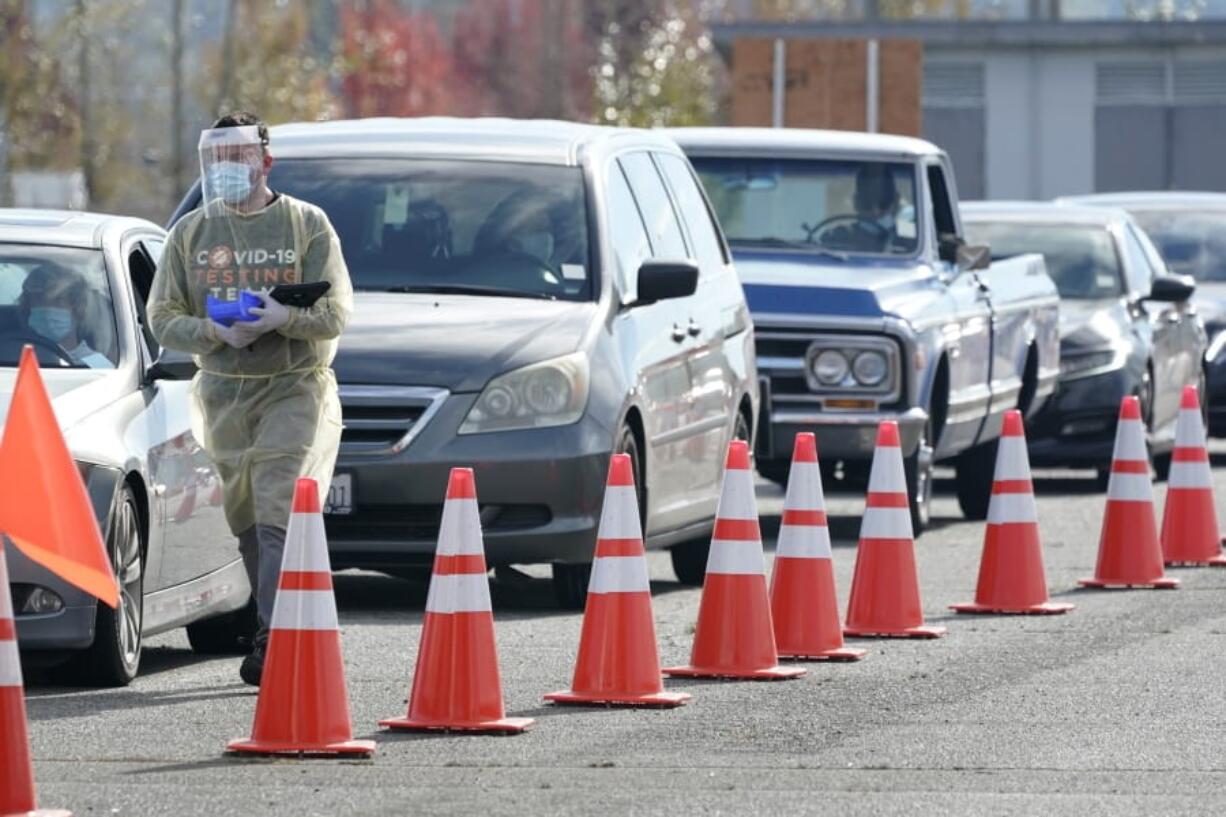 A worker wearing PPE  walks along a line of cars Oct. 28  at a King County COVID-19 testing site in Auburn. (ted s.