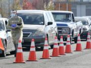 A worker wearing PPE  walks along a line of cars Oct. 28  at a King County COVID-19 testing site in Auburn. (ted s.