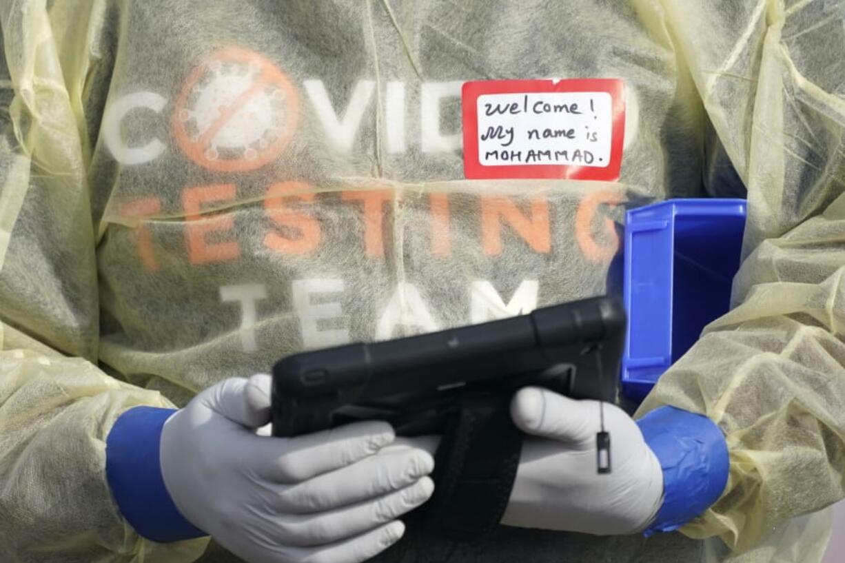 A worker wearing gloves, and other PPE holds a tablet computer as he waits to check people in, Wednesday, Oct. 28, 2020, at a King County coronavirus testing site in Auburn, Wash., south of Seattle. State health officials say that a new COVID-19 report released Wednesday shows an increase in coronavirus cases and hospitalizations throughout Washington state, and if not brought under control, officials said the spike could jeopardize progress toward reopening schools, strain the health care system and increase risks during the holiday season. (AP Photo/Ted S.