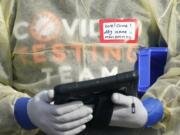 A worker wearing gloves, and other PPE holds a tablet computer as he waits to check people in, Wednesday, Oct. 28, 2020, at a King County coronavirus testing site in Auburn, Wash., south of Seattle. State health officials say that a new COVID-19 report released Wednesday shows an increase in coronavirus cases and hospitalizations throughout Washington state, and if not brought under control, officials said the spike could jeopardize progress toward reopening schools, strain the health care system and increase risks during the holiday season. (AP Photo/Ted S.