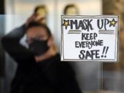 FILE - In this Tuesday, Nov. 17, 2020 file photo, manager Yllka Murati waits for a delivery driver to pick up takeout orders behind a partition displaying a sign to remind customers to wear a mask, at the Penrose Diner, in south Philadelphia. Despite the expected arrival of COVID-19 vaccines in just a few weeks, it could take several months -- probably well into 2021 -- before things get back to something close to normal in the U.S. and Americans can once again go to the movies, cheer at an NBA game or give Grandma a hug.