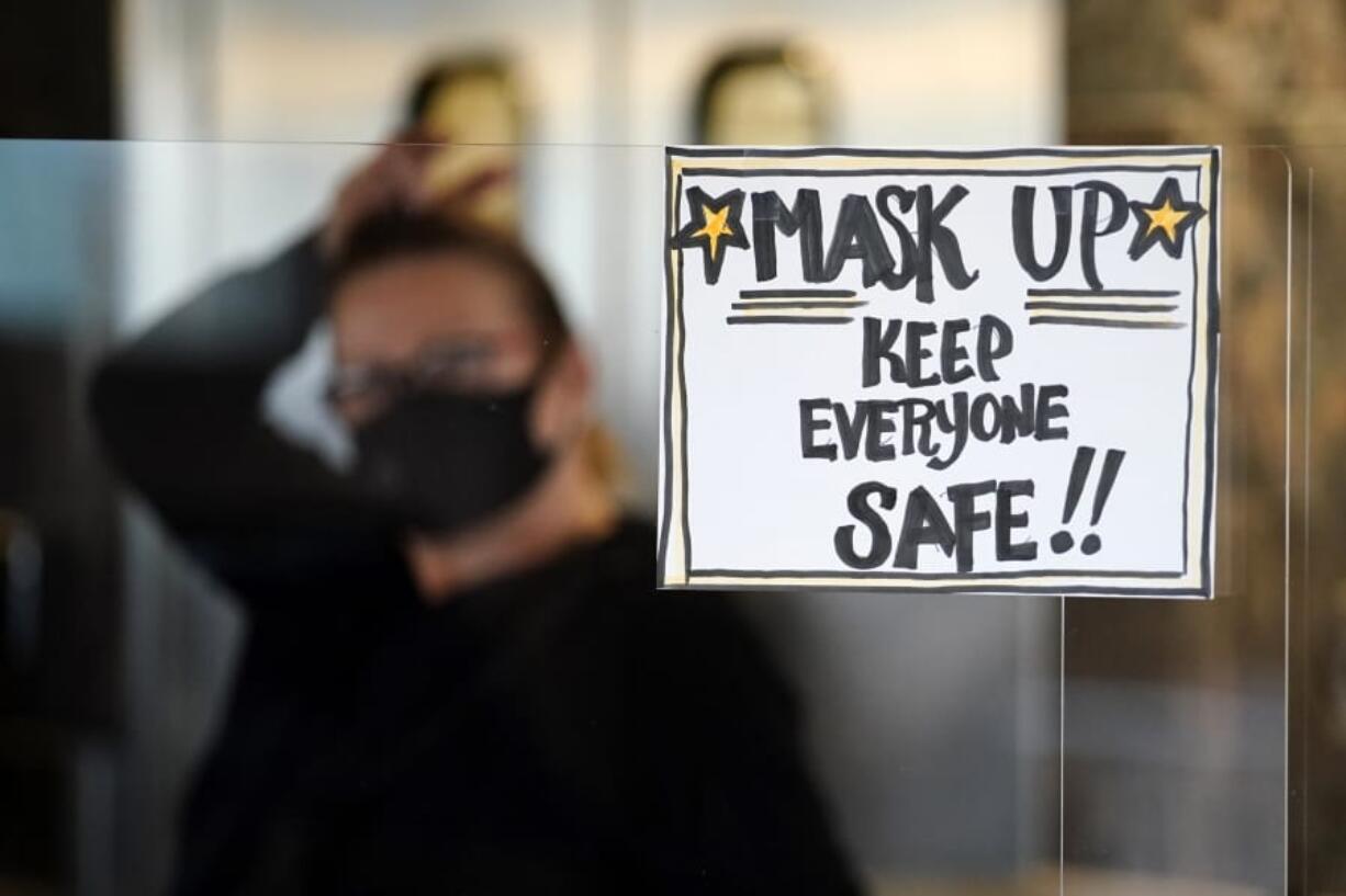 FILE - In this Tuesday, Nov. 17, 2020 file photo, manager Yllka Murati waits for a delivery driver to pick up takeout orders behind a partition displaying a sign to remind customers to wear a mask, at the Penrose Diner, in south Philadelphia. Despite the expected arrival of COVID-19 vaccines in just a few weeks, it could take several months -- probably well into 2021 -- before things get back to something close to normal in the U.S. and Americans can once again go to the movies, cheer at an NBA game or give Grandma a hug.