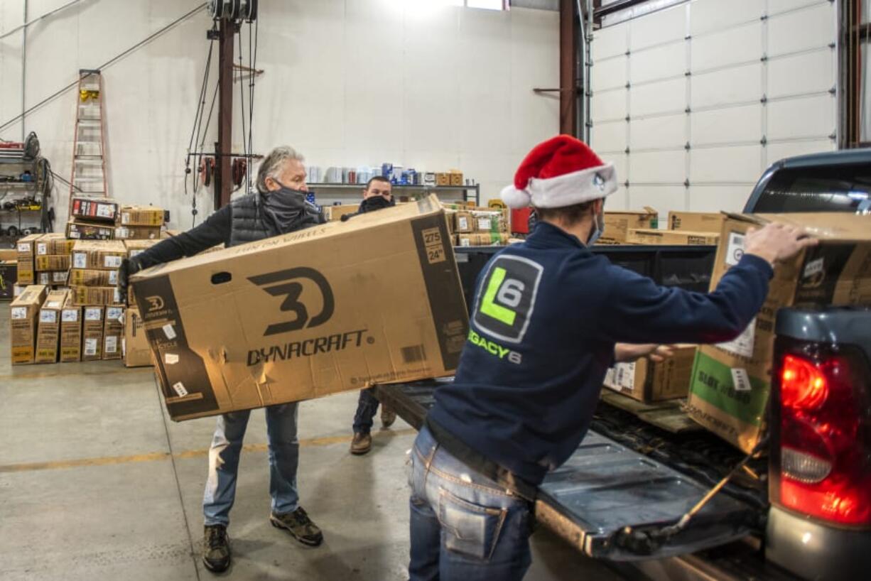 Rod Cook, left, helps load boxed-up bicycle kits into the back of a volunteer&#039;s pickup truck while Hayden Trent, right, repositions other boxes on Saturday morning at Taylor Transport in the Barberton area. Pre-registered volunteers drove though the warehouse to collect new bikes for home assembly. The bikes will be passed along to needy local families at Christmas.