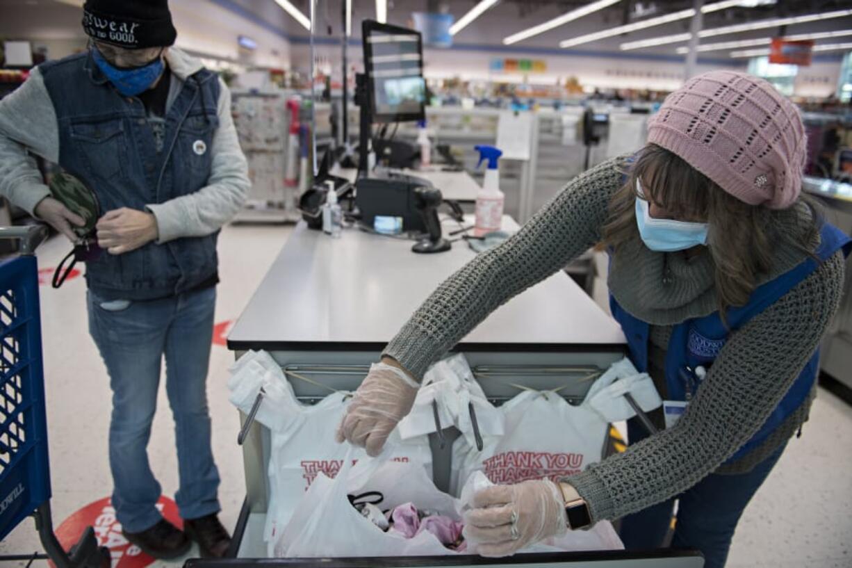 Patty Ashby of Vancouver, left, puts away her wallet as cashier Razija Zelknovic assists her with her plastic bags at the Orchards Goodwill. Single-use plastic bags will be banned under a new state law that was originally scheduled to take effect Jan. 1, prompting Goodwill and other retailers to switch to alternatives like paper bags. Gov. Jay Inslee announced last week that he would delay the start of the ban to the end of January, citing the COVID-19 pandemic.