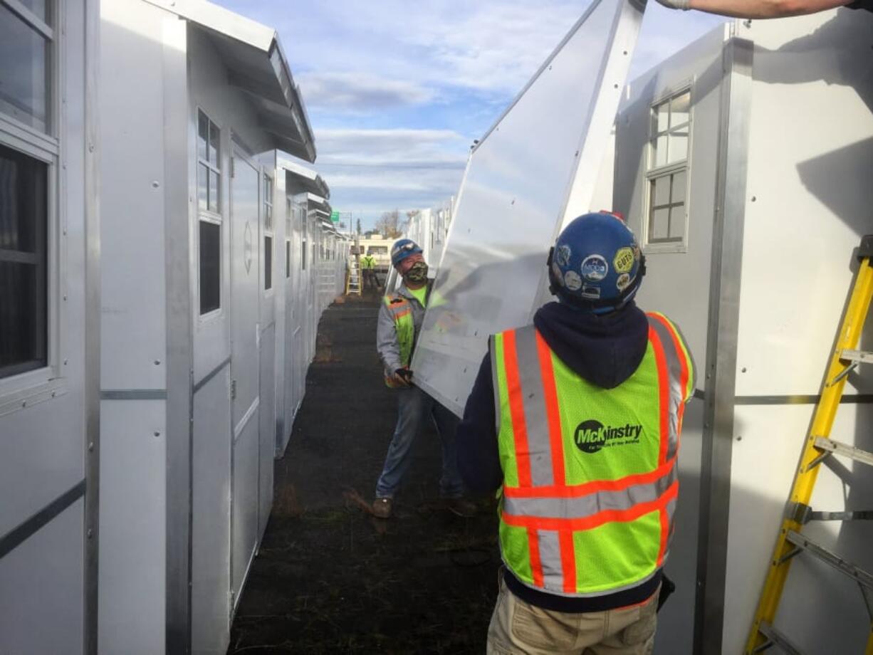 A side wall made of a rot-resistant plastic composite is carried by two crew members as they put together Pallet Shelter structures at a site in southeast Portland in December 2020.  A joint county-city agency purchased 100 of these  -- at $6,900 a piece -- from Everett-based Pallet.