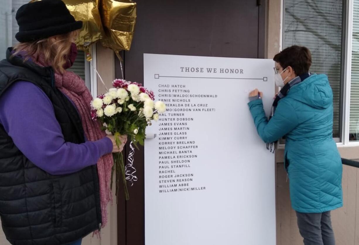 Laura Ellsworth writes a message on the memorial board set up Friday at St. Paul Lutheran Church in Vancouver, while Charlene Welch waits to leave flowers. Ellsworth and Welch, both from the Council for the Homeless, helped set up the board with the names of the homeless from the community who died in 2020.