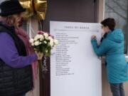 Laura Ellsworth writes a message on the memorial board set up Friday at St. Paul Lutheran Church in Vancouver, while Charlene Welch waits to leave flowers. Ellsworth and Welch, both from the Council for the Homeless, helped set up the board with the names of the homeless from the community who died in 2020.