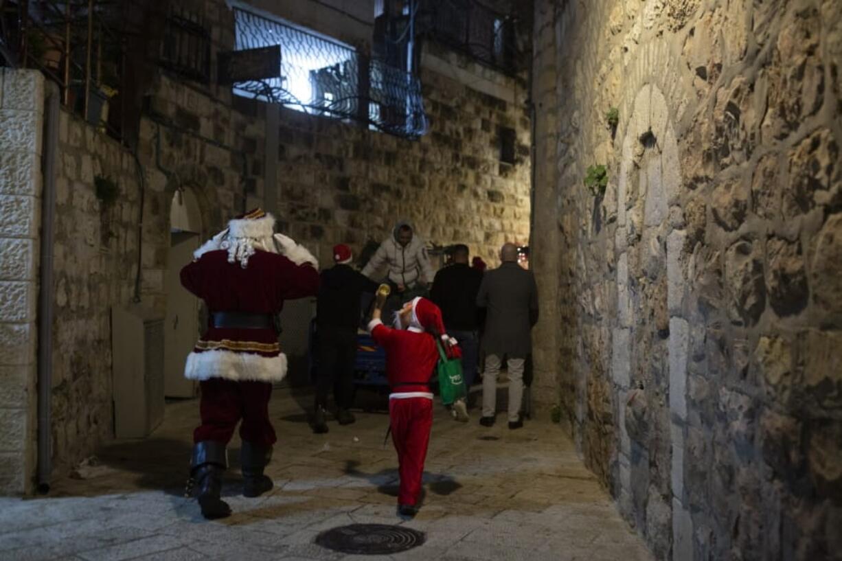 A child dressed as Santa Claus, right, rings a bell for Jerusalem&#039;s Santa Claus as they walk with volunteers from a Catholic men&#039;s group distributing presents to children on Christmas Eve in the Christian Quarter of the Old City of Jerusalem, Thursday, Dec. 24, 2020.  With the coronavirus dampening Christmas celebrations this year, the men&#039;s group organized gifts to families free of charge.