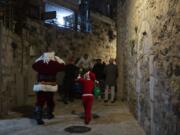 A child dressed as Santa Claus, right, rings a bell for Jerusalem&#039;s Santa Claus as they walk with volunteers from a Catholic men&#039;s group distributing presents to children on Christmas Eve in the Christian Quarter of the Old City of Jerusalem, Thursday, Dec. 24, 2020.  With the coronavirus dampening Christmas celebrations this year, the men&#039;s group organized gifts to families free of charge.