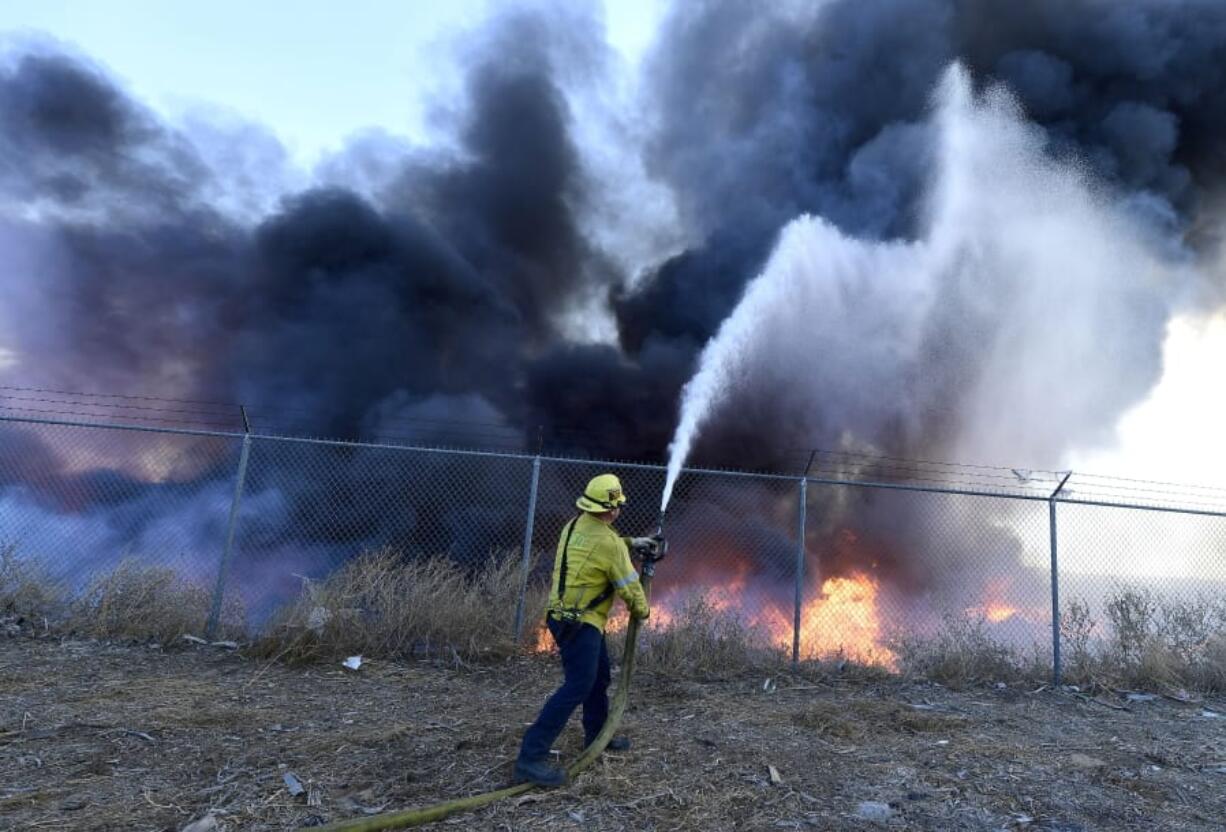 A firefighter battles a mulch and pallet fire burning out of control, fanned by Santa Ana winds in and around a recycling yard near Wilson Street and Fleetwood Drive in Riverside, Calif., Thursday, Dec. 3, 2020. Firefighters from both Riverside and San Bernardino County, along with assistance from Colton, Rialto and Riverside City Fire fought the blaze.