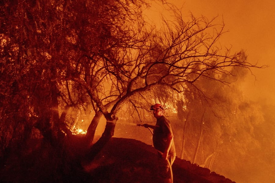 Bruce McDougal hoses down vegetation while working to save his home from the Bond Fire burning though the Silverado community in Orange County, Calif., on Thursday, Dec. 3, 2020.