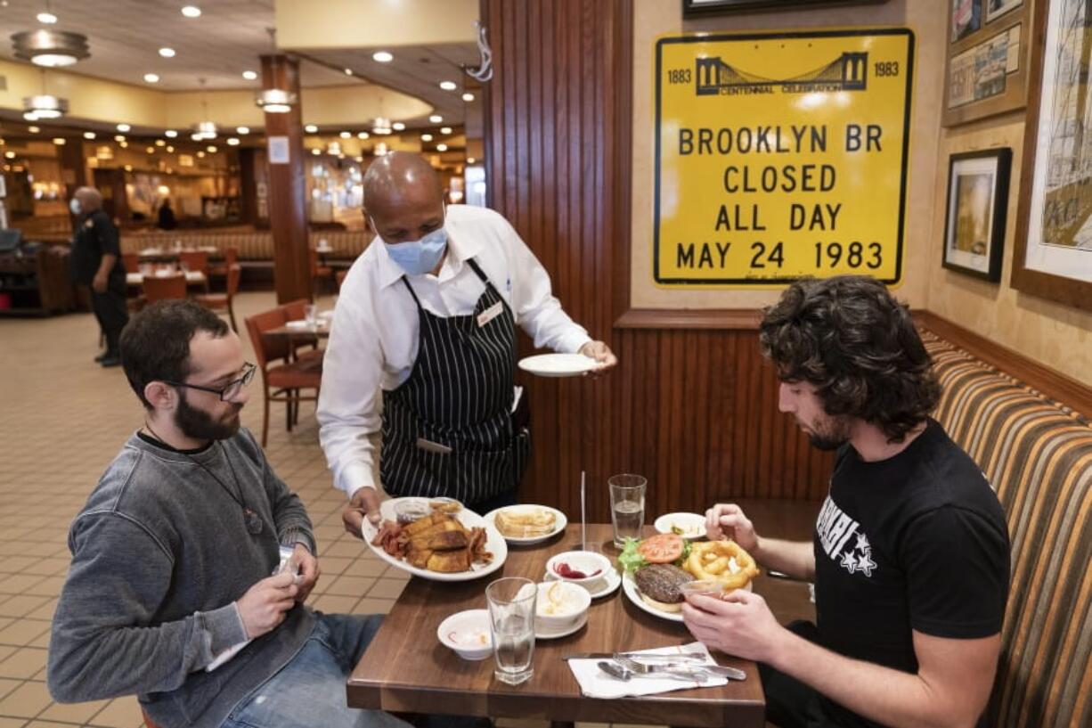 FILE- In this Sept. 30, 2020 file photo, waiter Lenworth Thompson serves lunch to David Zennario, left, and Alex Ecklin at Junior&#039;s Restaurant in New York.  The U.S. services sector, where most Americans work, registered its fifth consecutive month of expansion in October 2020.