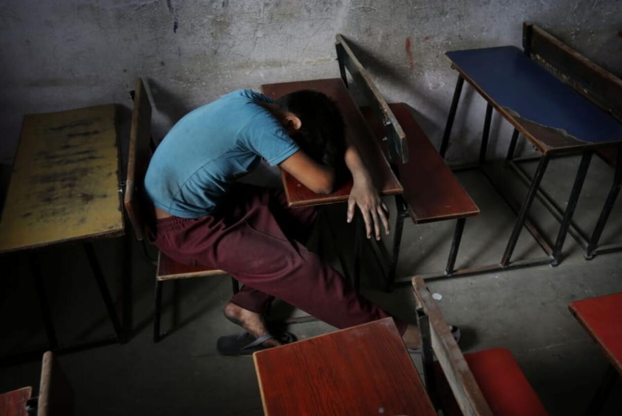 FILE - In this Tuesday, June 11, 2013, file photo, a bonded child laborer rests on a school desk in a safe house after being rescued during a raid by workers from Bachpan Bachao Andolan, or Save Childhood Movement, at a garments factory in New Delhi, India. With classrooms shuttered and parents losing their jobs, many children are working in farms, illegal factories, brick kilns and roadside stalls, reversing decades of progress to stop child labor. In rural India, a nationwide lockdown imposed in March, 2020, pushed millions of people into poverty, encouraging trafficking of children from villages into cities for cheap labor.