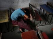 FILE - In this Tuesday, June 11, 2013, file photo, a bonded child laborer rests on a school desk in a safe house after being rescued during a raid by workers from Bachpan Bachao Andolan, or Save Childhood Movement, at a garments factory in New Delhi, India. With classrooms shuttered and parents losing their jobs, many children are working in farms, illegal factories, brick kilns and roadside stalls, reversing decades of progress to stop child labor. In rural India, a nationwide lockdown imposed in March, 2020, pushed millions of people into poverty, encouraging trafficking of children from villages into cities for cheap labor.