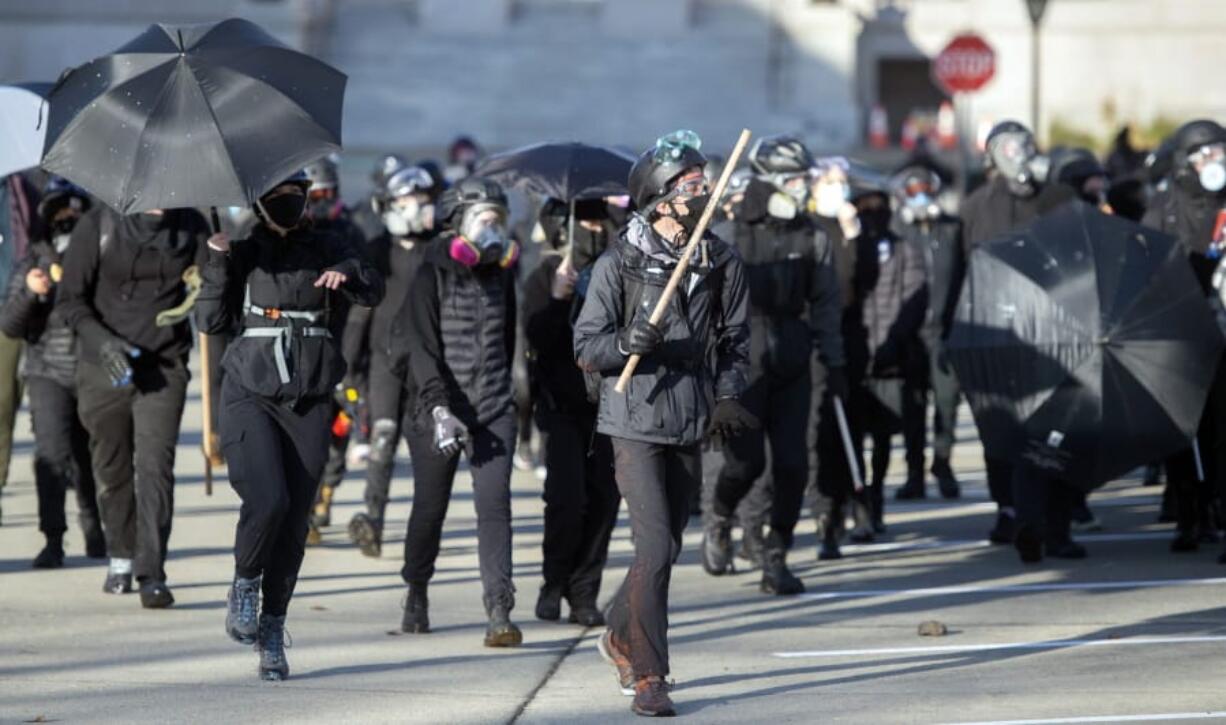 A large group of black clad protesters marched through the Washington Capitol Campus and downtown Olympia, Wash., clashing with supporters of President Donald Trump and threatening bystanders, Saturday, Dec. 12, 2020. Police in Olympia declared a riot early Saturday afternoon and arrested at least one person as groups with different points of view held simultaneous protests.