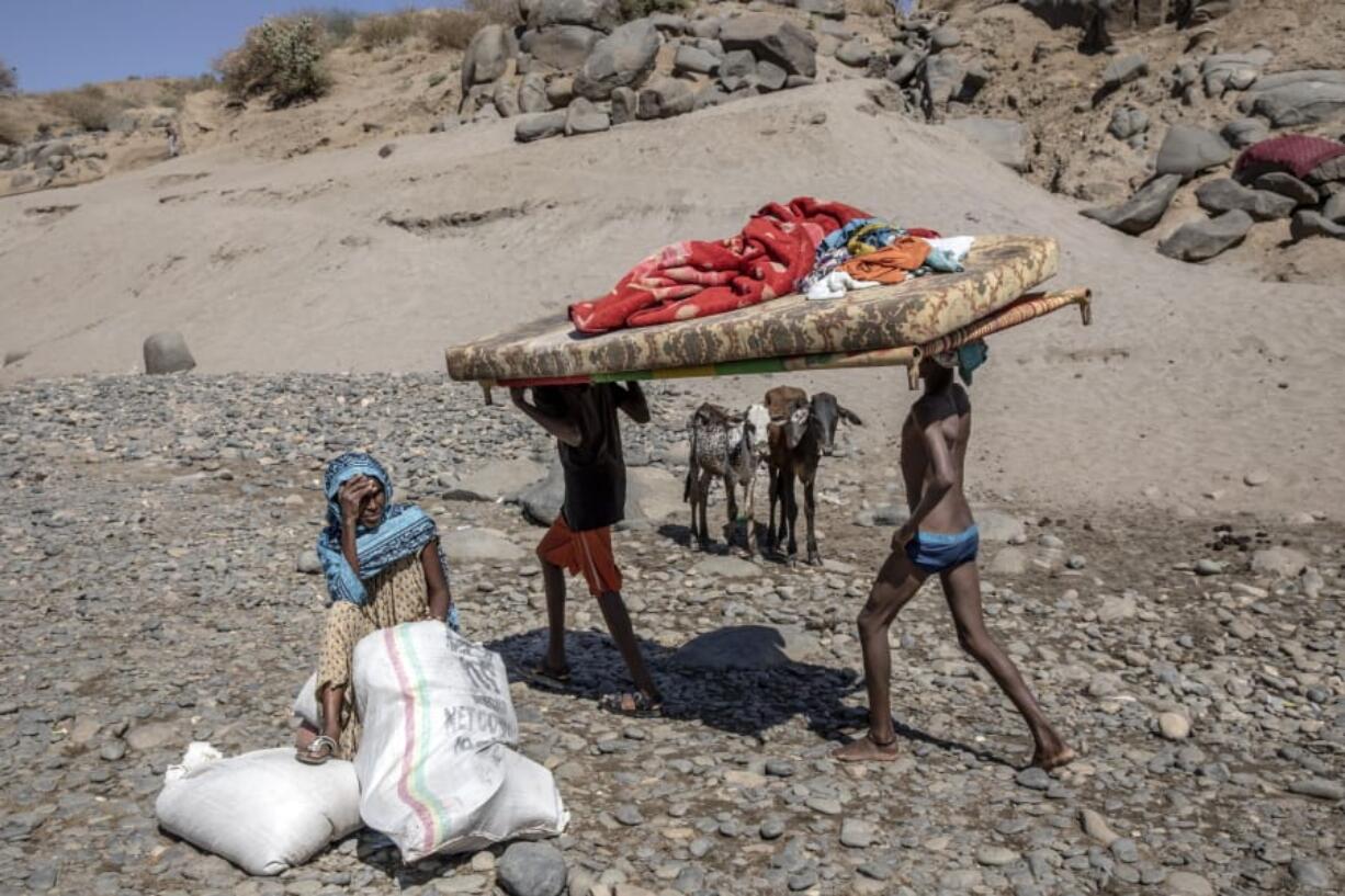 Tigray refugees who fled the conflict in the Ethiopia&#039;s Tigray carry their furniture on the banks of the Tekeze River on the Sudan-Ethiopia border, in Hamdayet, eastern Sudan, Tuesday, Dec. 1, 2020. The elderly woman waits for her family with their two cows they brought with them at center.