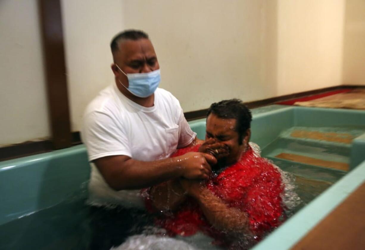 Pastor Luke Jesse of the First Marshallese Throne in Jouj church wears a mask as he baptizes Danny Baro on Sunday, Nov. 22, 2020, in Noel, Mo. After the coronavirus swept through the town of about 1,800 people, the First Marshallese Throne in Jouj and four other churches that worship at the building of the Community Baptist Church experienced a faith revival with an estimated 50 baptisms in three months.