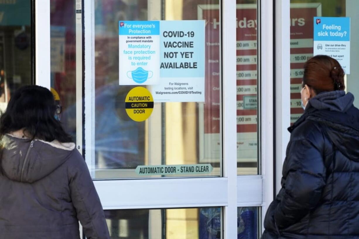 FILE - In this Dec. 4, 2020, file photo, customers wear a mask as they check out information signs that a COVID-19 vaccine is not yet available at Walgreens in Northbrook, Ill. A new poll released Wednesday, Dec. 9, from The Associated Press-NORC Center for Public Affairs Research, find only about half of Americans are ready to roll up their sleeves for COVID-19 vaccines even as states frantically prepare to begin months of vaccinations that could end the pandemic. (AP Photo/Nam Y.