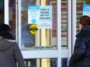 FILE - In this Dec. 4, 2020, file photo, customers wear a mask as they check out information signs that a COVID-19 vaccine is not yet available at Walgreens in Northbrook, Ill. A new poll released Wednesday, Dec. 9, from The Associated Press-NORC Center for Public Affairs Research, find only about half of Americans are ready to roll up their sleeves for COVID-19 vaccines even as states frantically prepare to begin months of vaccinations that could end the pandemic. (AP Photo/Nam Y.