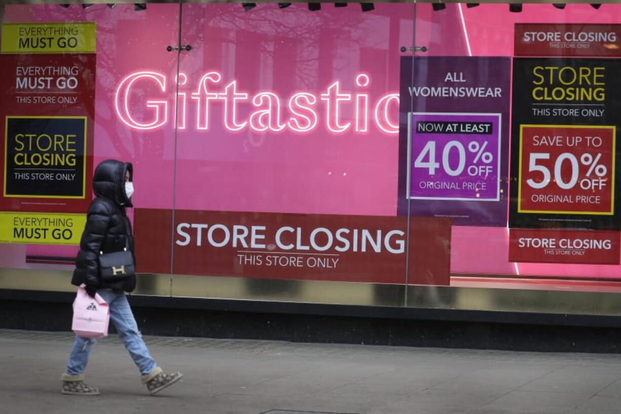 A woman walks past a Sale signs in the window of a closed shop on Oxford Street in London, Saturday, Dec. 26, 2020. London is currently in Tier 4 with all non essential retail shops closed and people have been asked to stay at home, on what is usually one of the busiest retail days of the year with the traditional Boxing Day sales in shops.