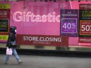 A woman walks past a Sale signs in the window of a closed shop on Oxford Street in London, Saturday, Dec. 26, 2020. London is currently in Tier 4 with all non essential retail shops closed and people have been asked to stay at home, on what is usually one of the busiest retail days of the year with the traditional Boxing Day sales in shops.