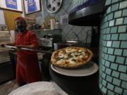 Eugenio Iorio wears a face mask to curb the spread of COVID-19 as he bakes a pizza at a restaurant in Naples, Italy.